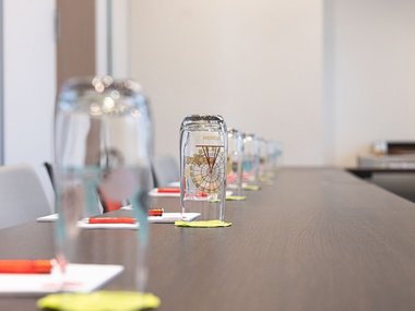 Eingedeckter Tagungstisch mit Wasserglas, Blöcken und Stiften 