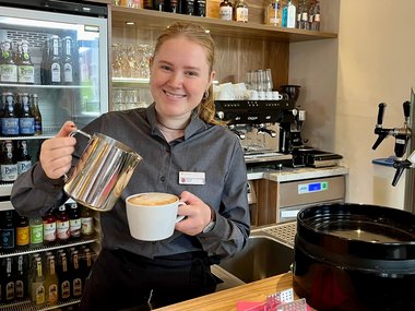 Ein Frau schüttet Milchschaum in einen Kaffee