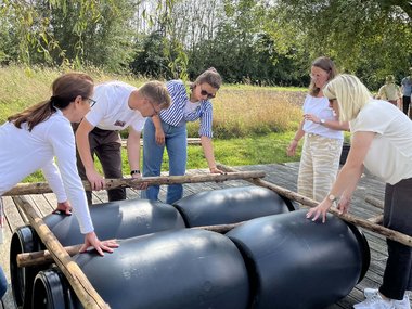 Menschen, die mit Hölzern und Fässern ein Floß bauen